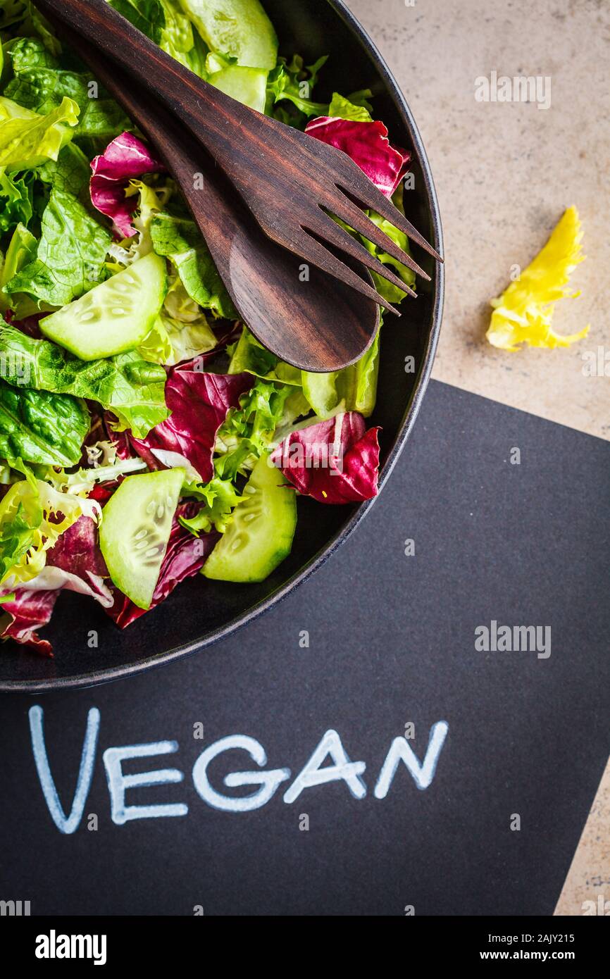 Vegan food concept. Green vegetable salad in a black plate and a notebook with the word vegan, copy space. Stock Photo