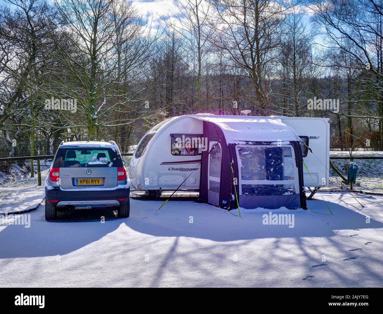 A female caravanner opens a window in a Swift Challenger Sport 514 caravan, parked next to a Skoda Yeti tow car on a sunny winter day after a fall of Stock Photo