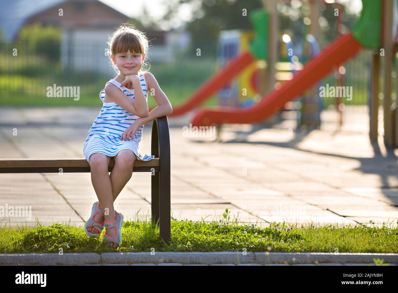 Cute young girl in short dress sitting alone outdoors on playground bench on sunny summer day Stock Photo Alamy