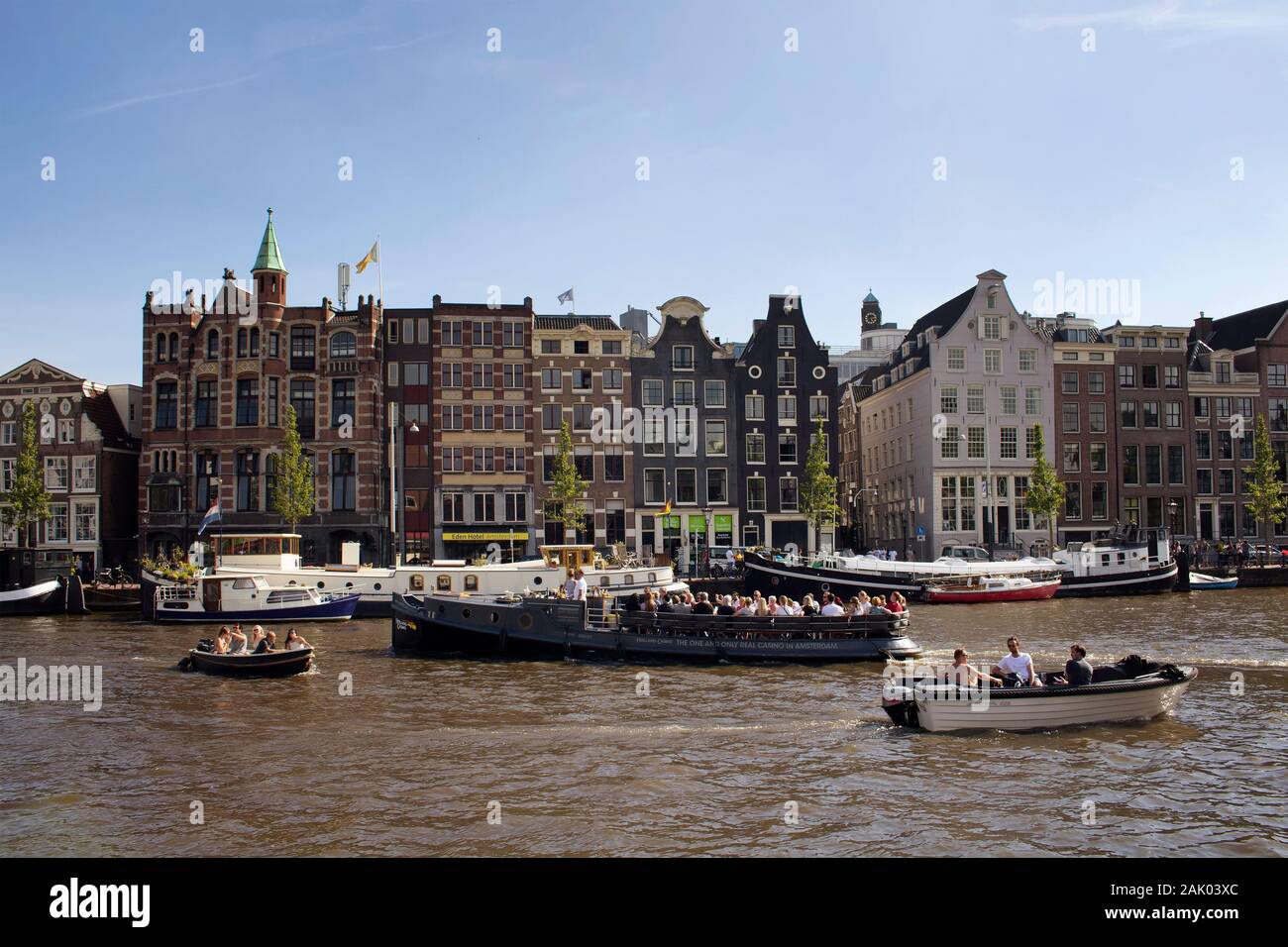 View of people riding open boats in Amstel river doing canal cruise tours. Historical, traditional and typical buildings are in the background. It is Stock Photo