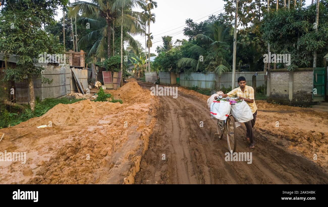 Amarpur, Tripura, India - December 2018: A man walks with his cycle loaded with luggage on the terrible, muddy and slushy roads in rural Tripura. Stock Photo