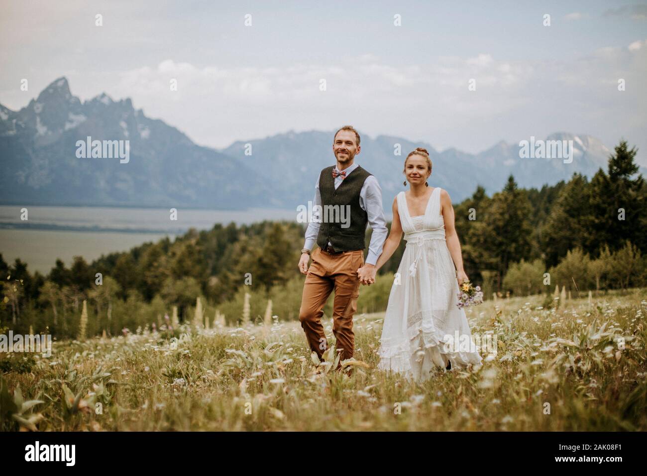 Bride and Groom walk through wildflowers in front of Teton mountains Stock Photo