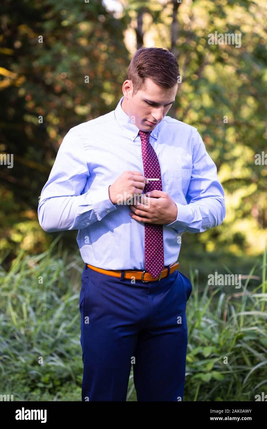 Young man in suit stands outside adjusting tie. Stock Photo