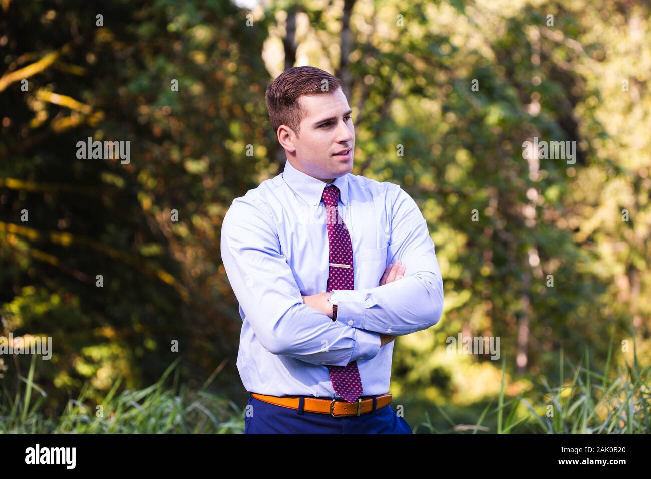 Young man in suit stands confidently outside with arms crossed. Stock Photo