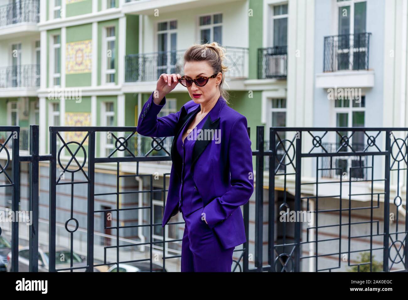 A portrait of a blond woman wearing in a purple suit and glasses poses ...