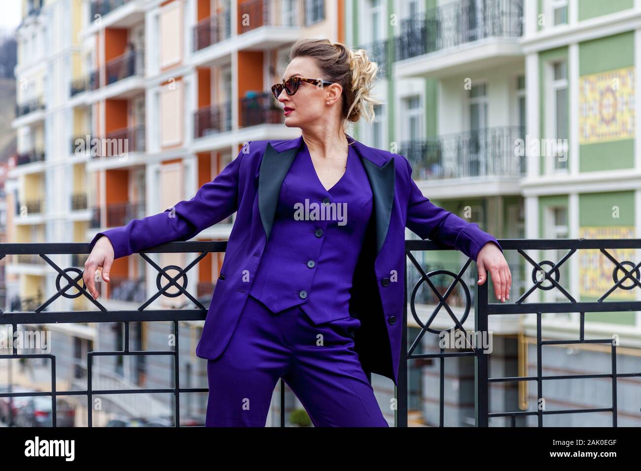 A portrait of a blond woman wearing in a purple suit and glasses poses ...