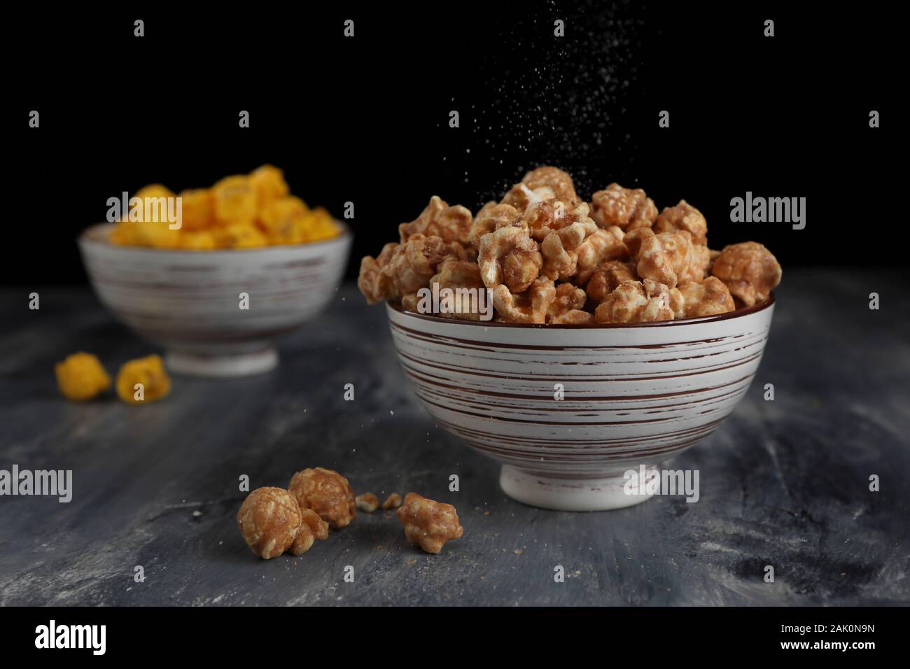 A close up of salt sprinkling over caramel popcorn in a bowl taken in the studio. Stock Photo