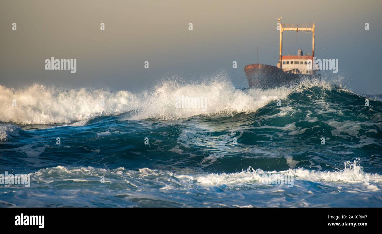 Abandoned ship in the stormy sea with big wind waves during sunset. Stock Photo