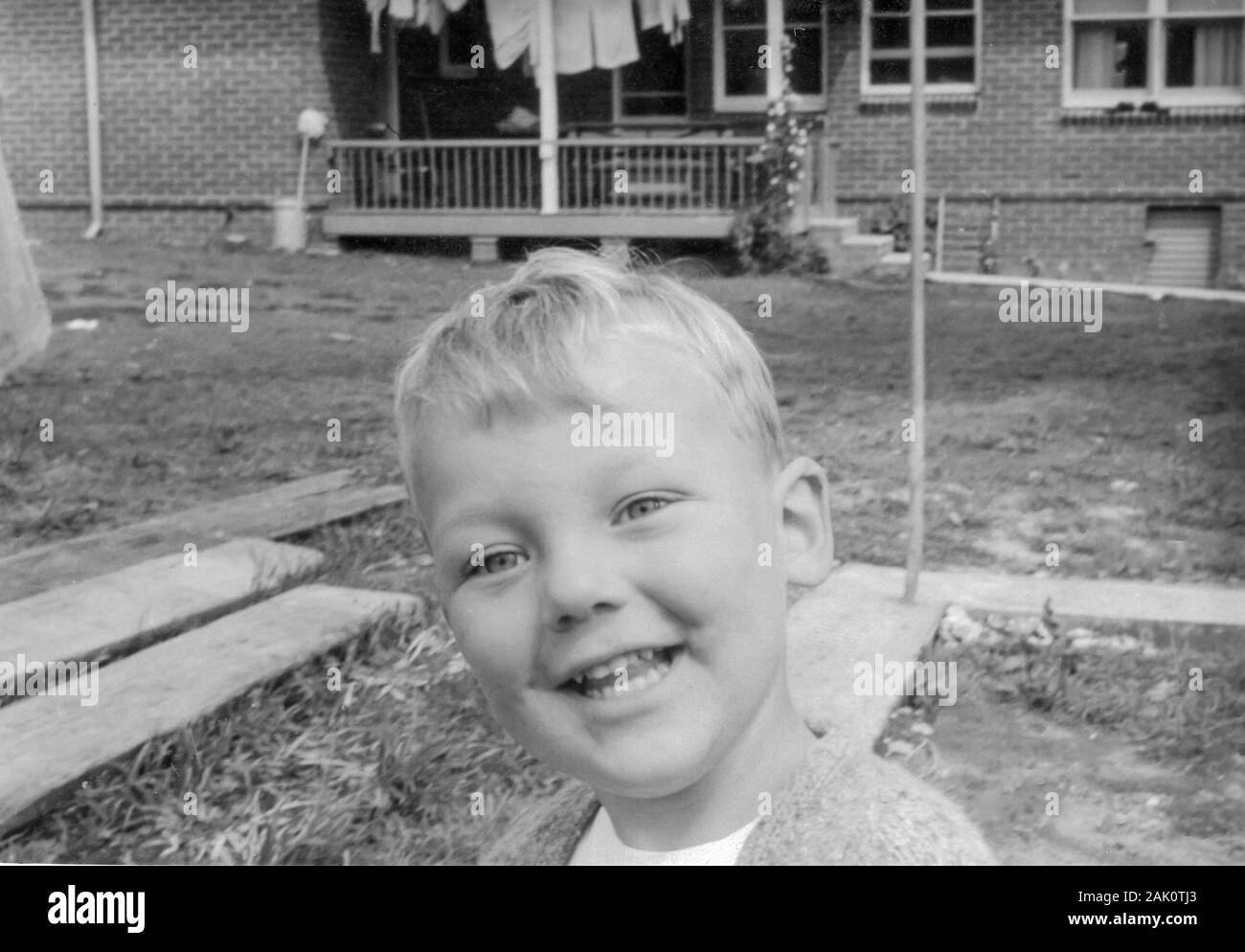 A close up black and white image of a young blonde haired boy aged three in his backyard smiling at the camera in Sydney in 1963 Stock Photo