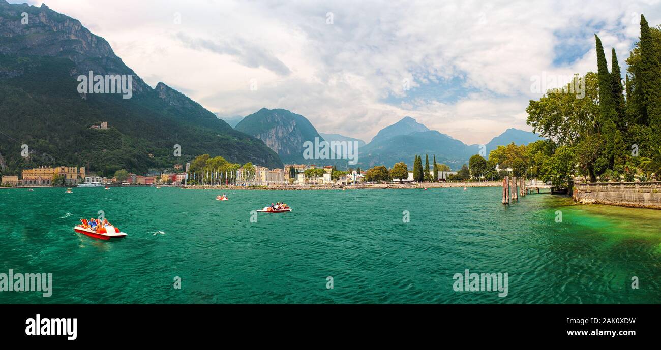 Coast of emerald lake Lago di Garda near the city Riva del Garda, Italy, mountains (alps) and cloudy sky in the background Stock Photo