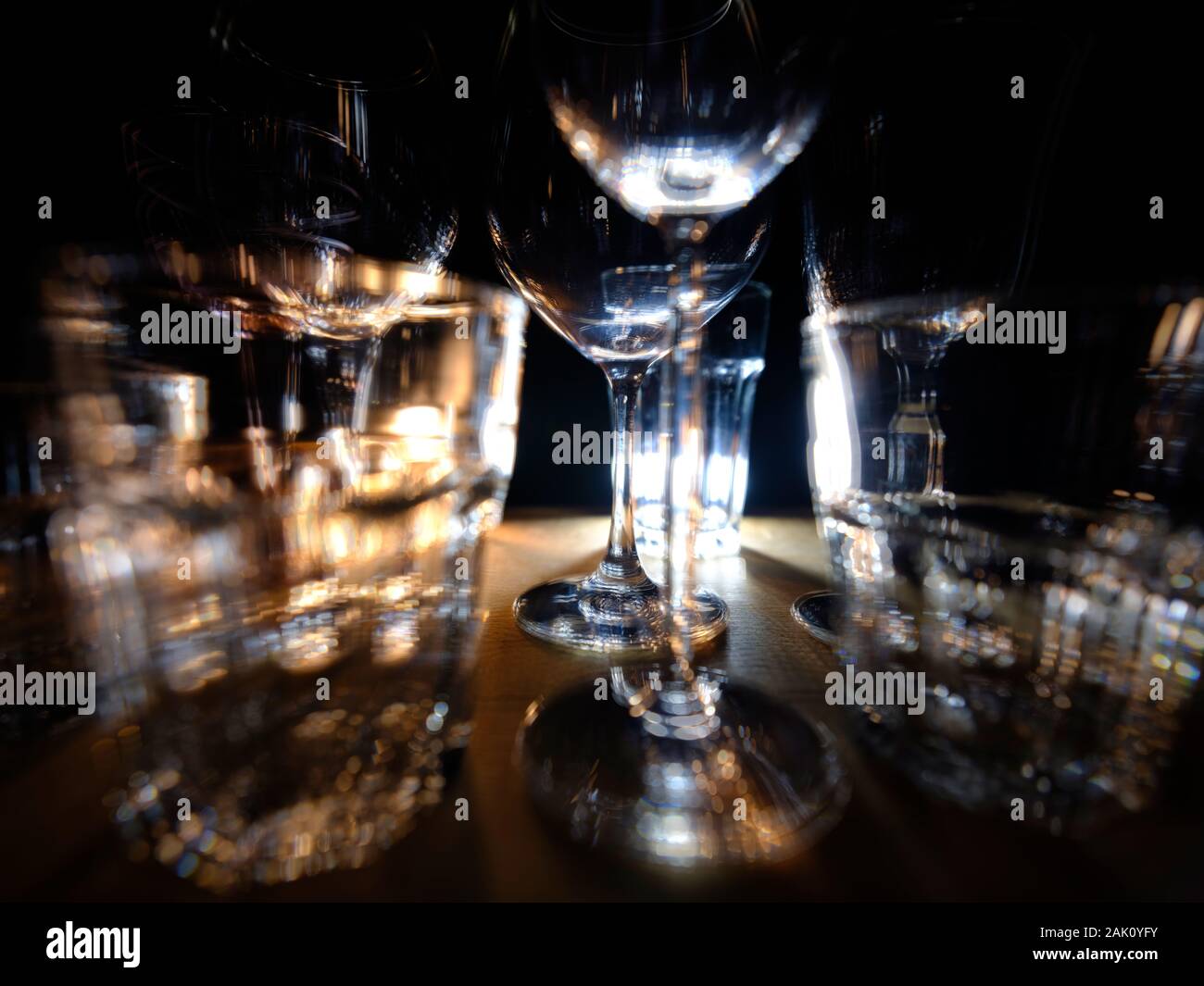 Close ups of wine-, long drink- and spirits-glasses on a wooden shelve in a bar environment, in fron of a dark background, illuminated by colorful spo Stock Photo