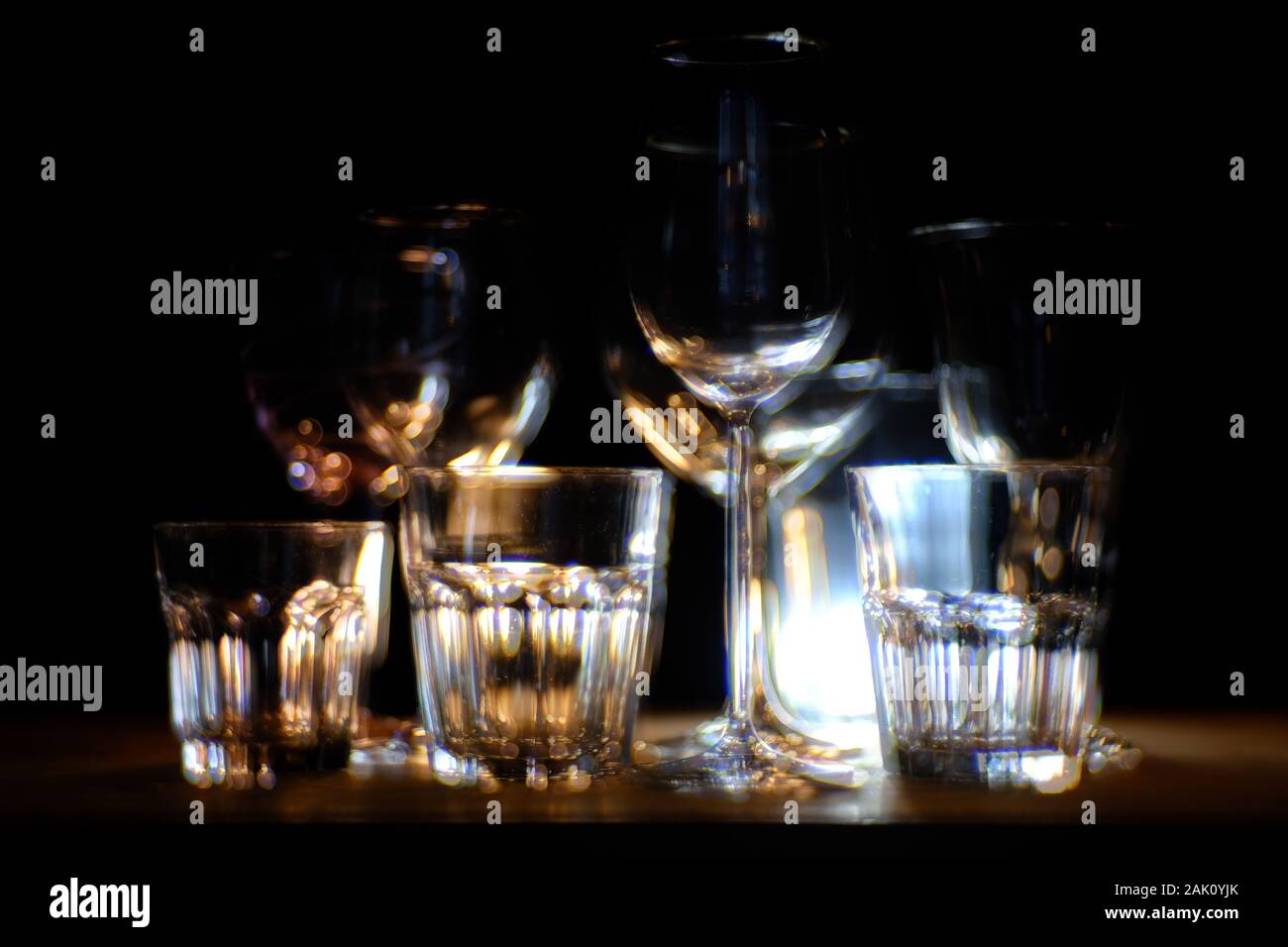 Close ups of wine-, long drink- and spirits-glasses on a wooden shelve in a bar environment, in fron of a dark background, illuminated by colorful spo Stock Photo