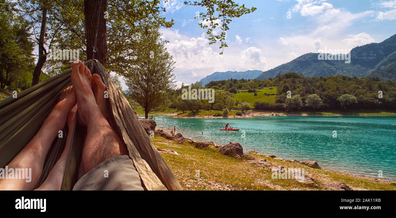 Couple resting in hammock (view from hammock) on sunny beach of mountain lake, blue sky with white clouds Stock Photo