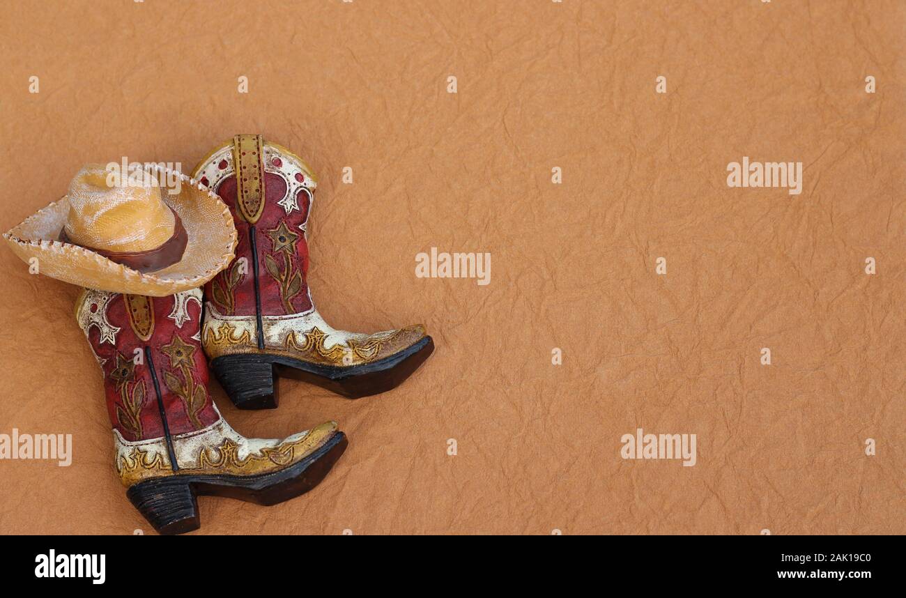 Cowboy boots and hat laying on a tan background with writing space Stock Photo