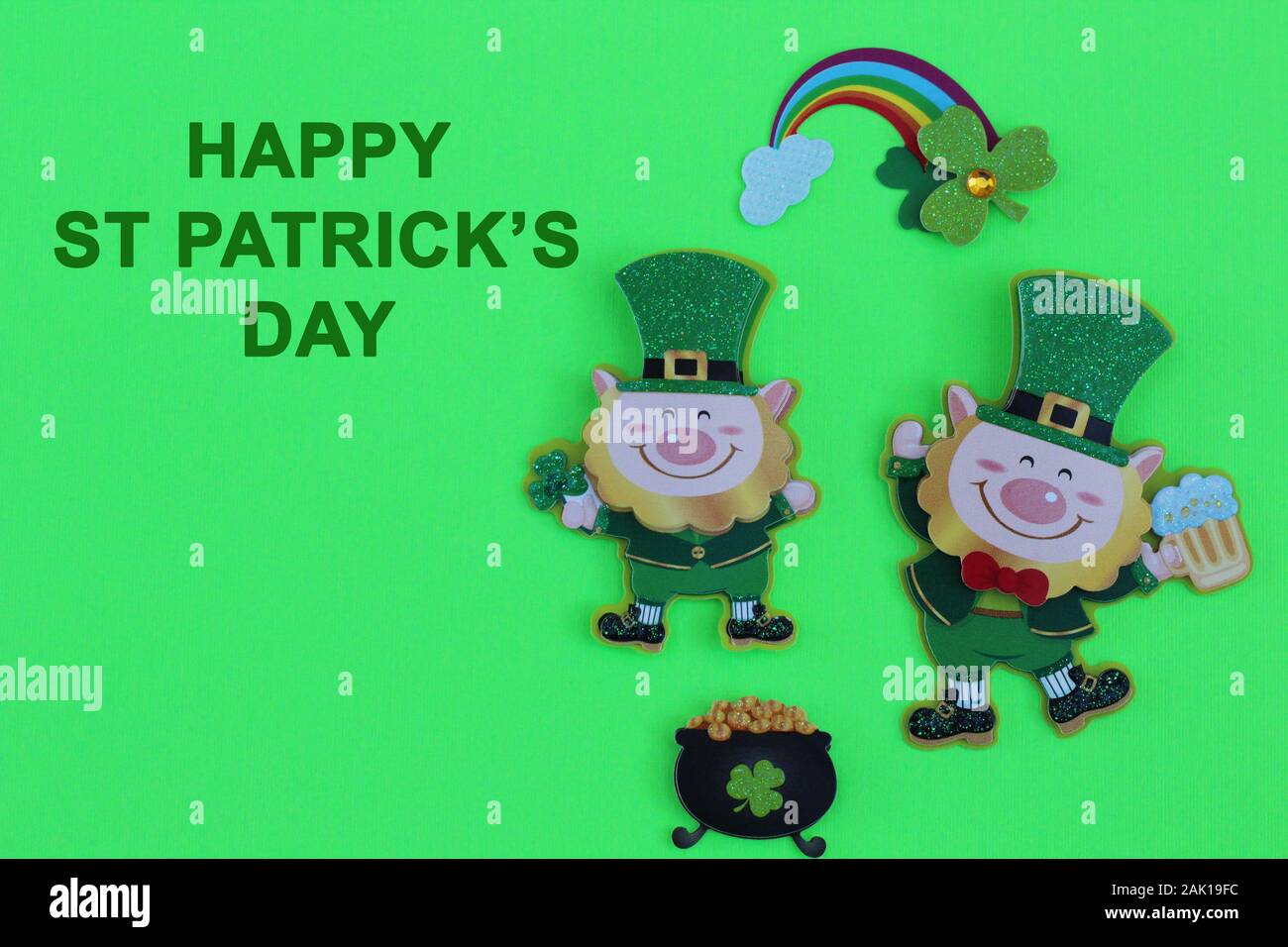 leprechauns holding mug of beer next to a black pot of gold and a rainbow with happy st Patricks day in green text on a green background Stock Photo