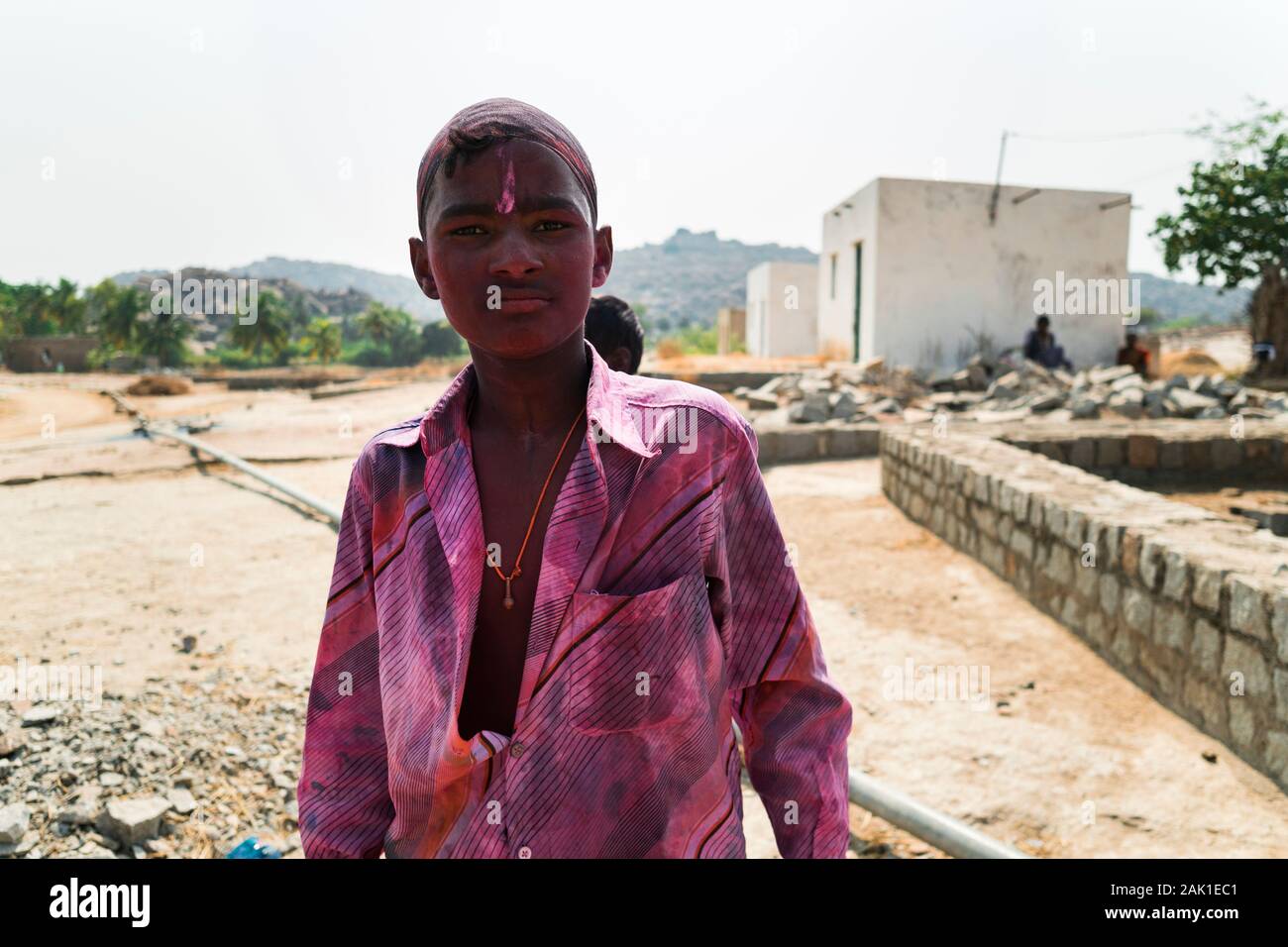 Hampi, India - April 07, 2019: Young indian guy painted in pink pigments celebrating Holy Festival in rural village in Hanuman Halli, Karnataka, India Stock Photo
