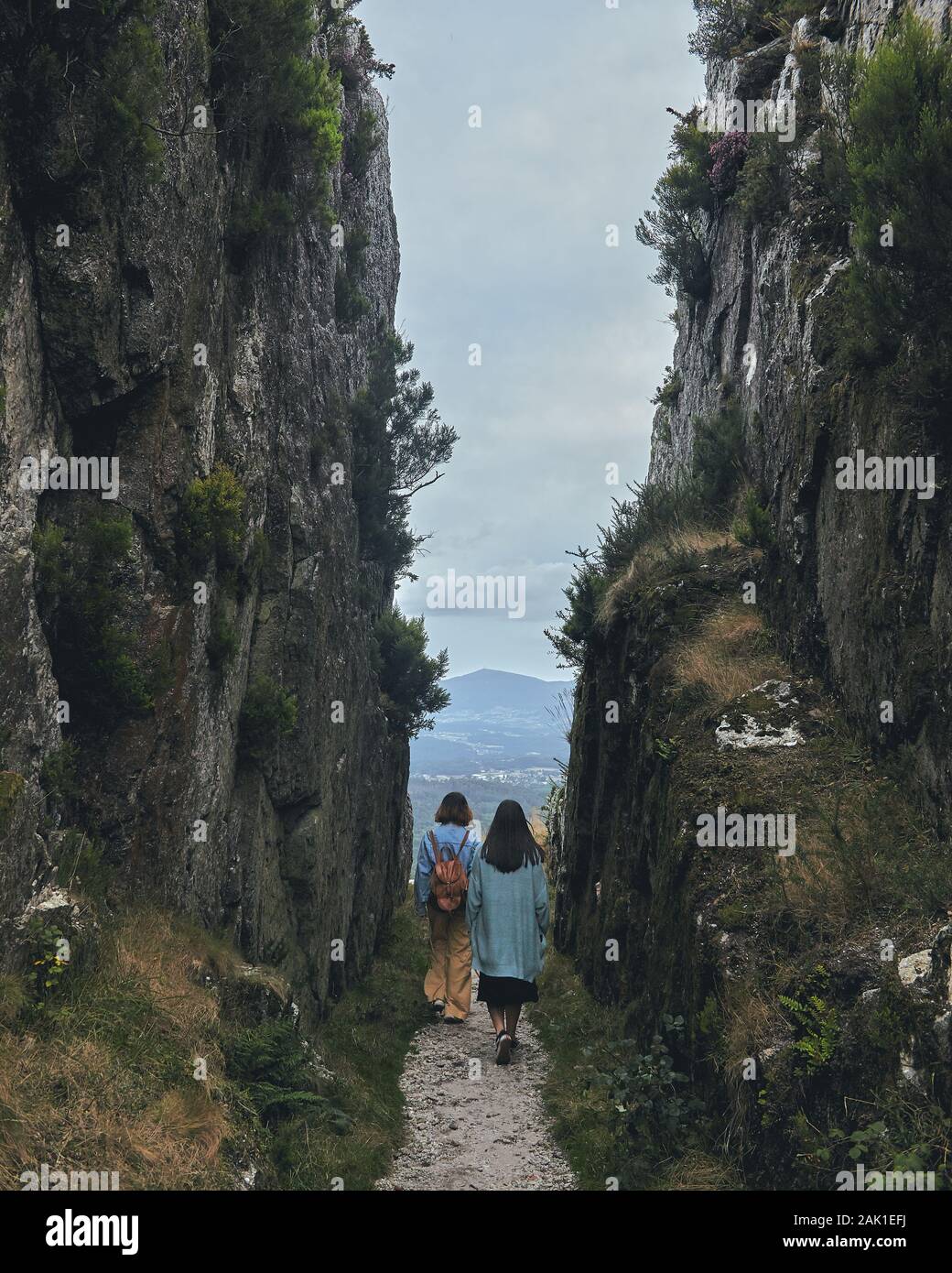 Two young women walking through a path between mountains cloudy day Stock Photo