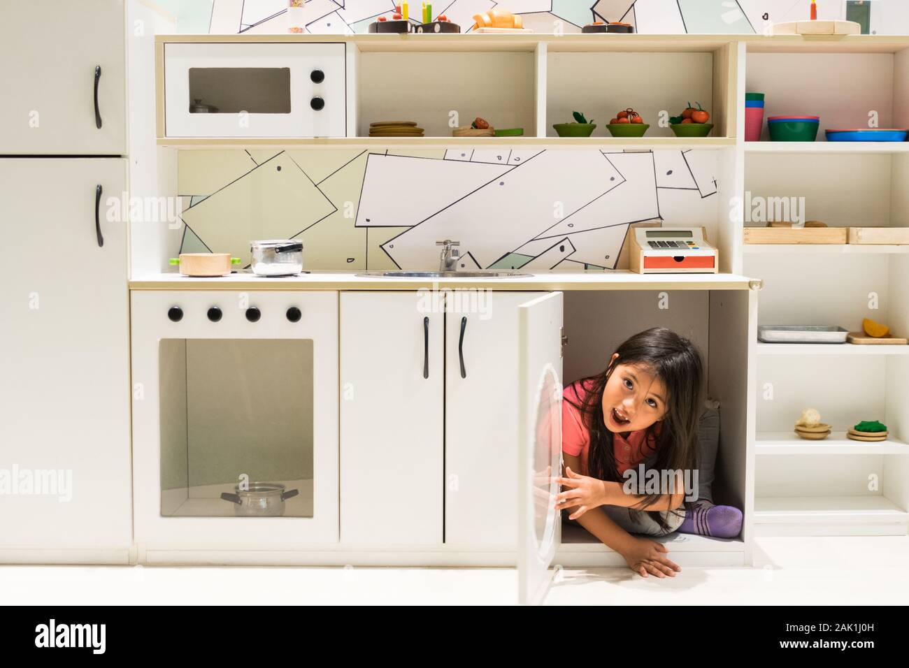 Beautiful girl coming out of the kitchen cupboard for girls Stock Photo