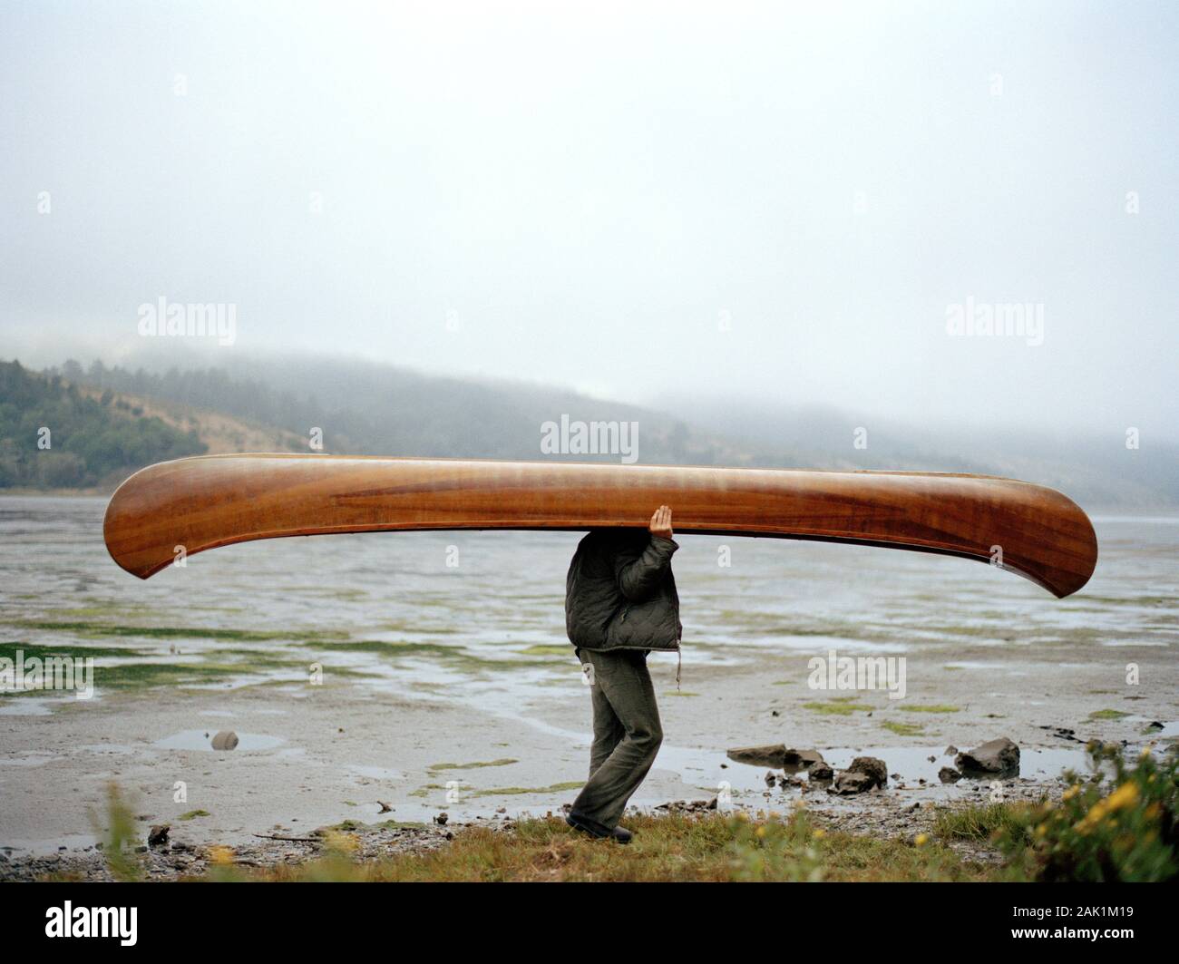 Man carrying canoe beside river Stock Photo