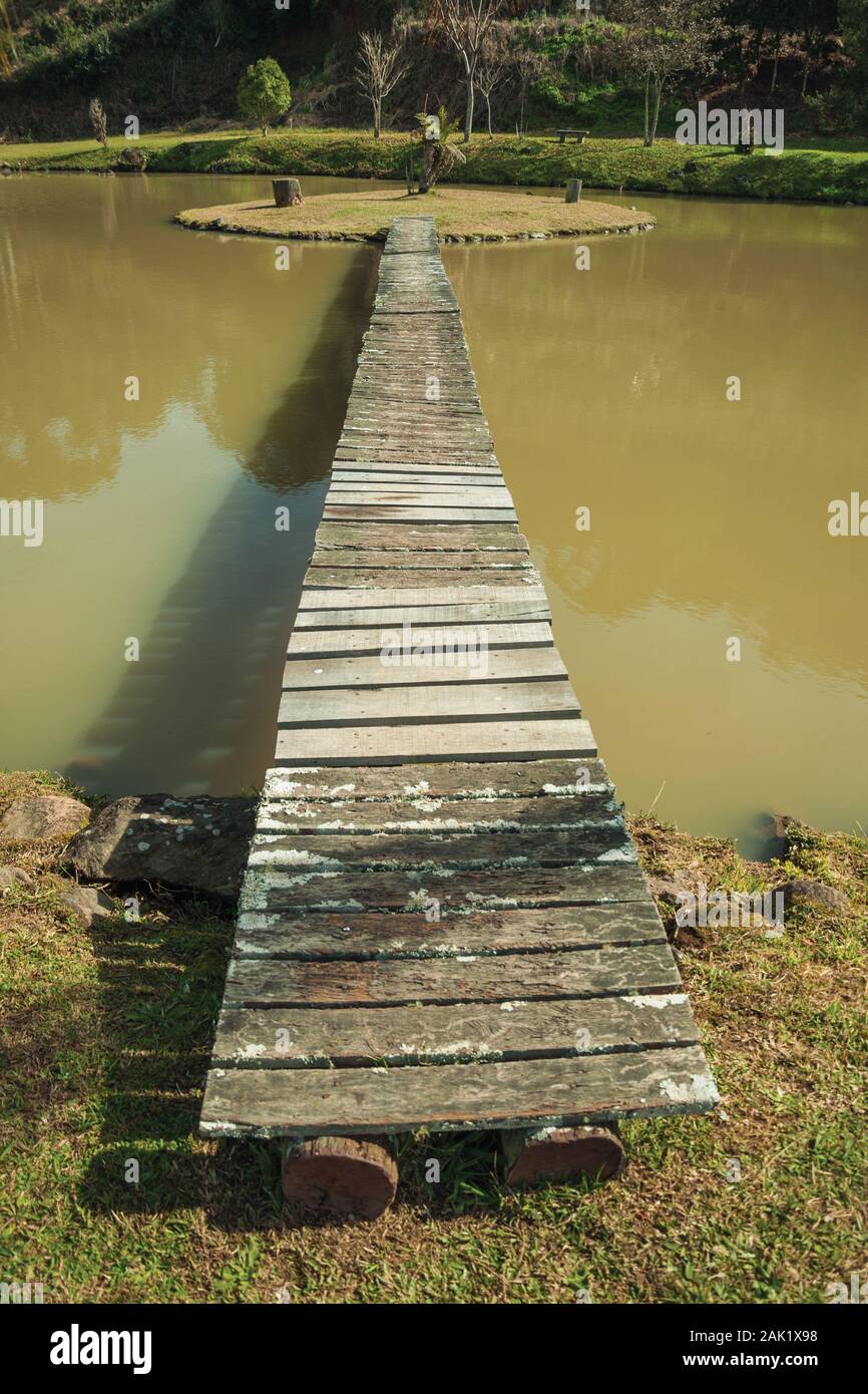 Wooden walkway going to a small island in pond from a garden with palm trees near Bento Goncalves. A wine producing country city in southern Brazil. Stock Photo