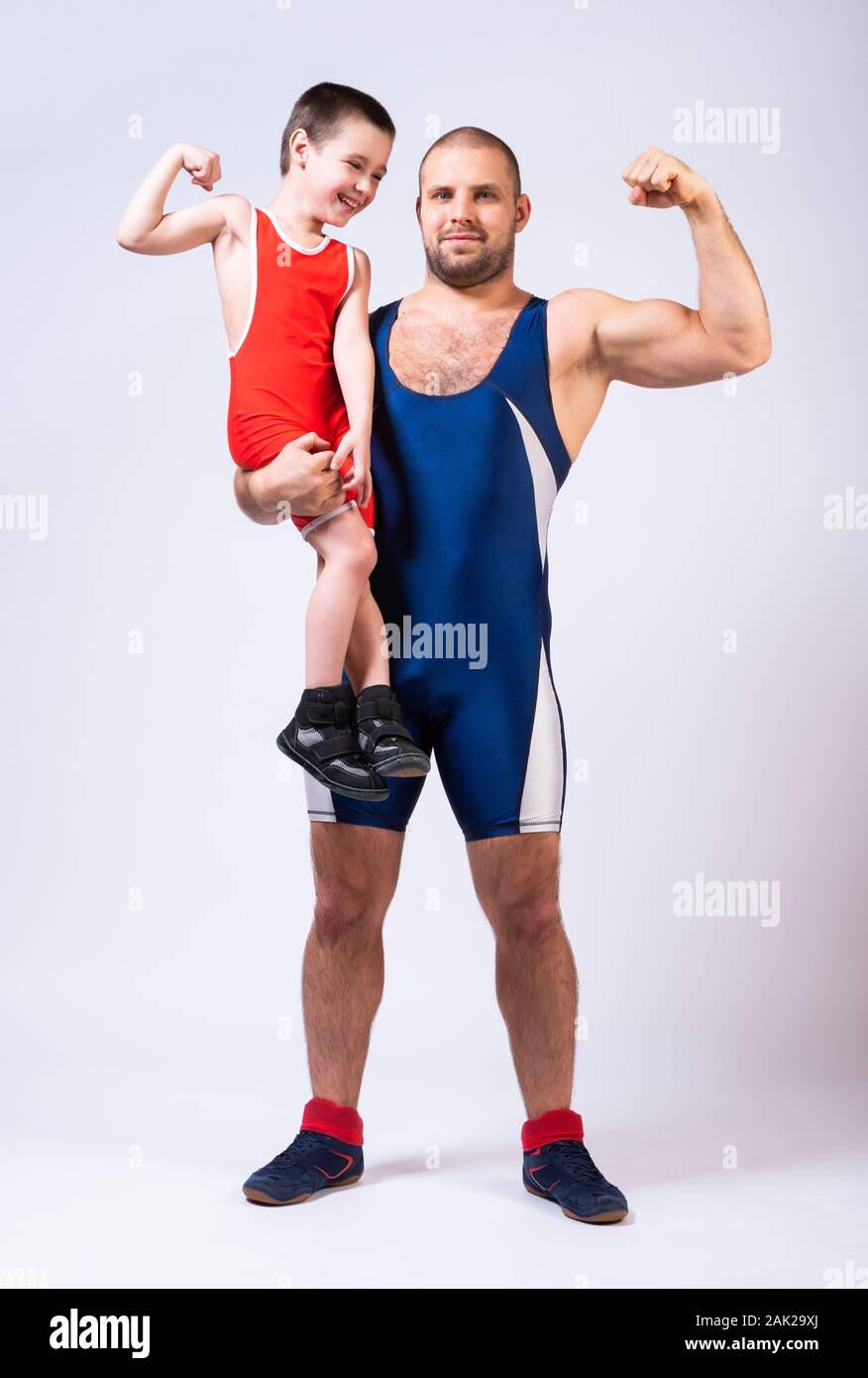 Men in wrestling tights holds the boy with one hand and they both