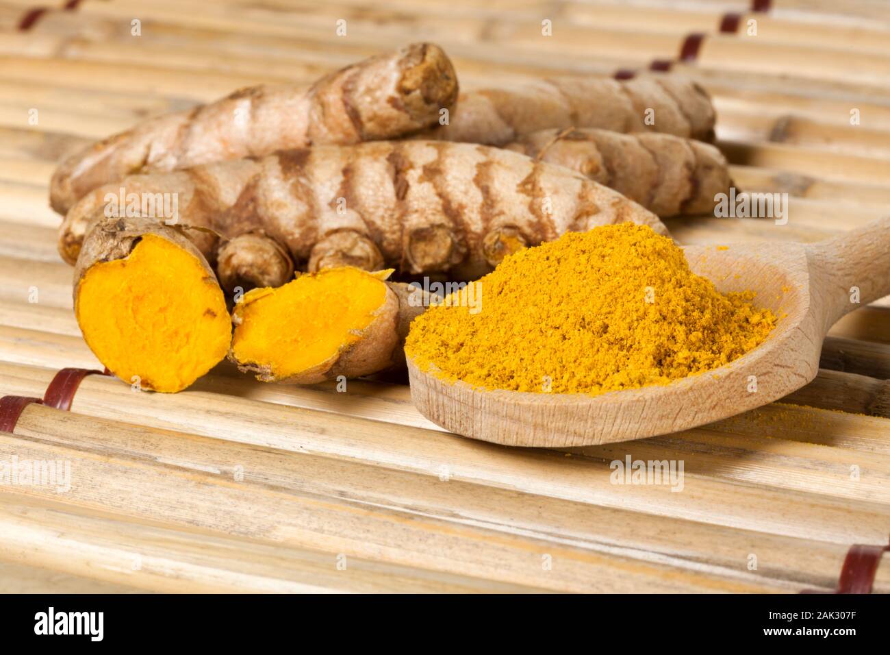 Ground turmeric on wooden spoon and turmeric roots on bamboo mat Stock Photo