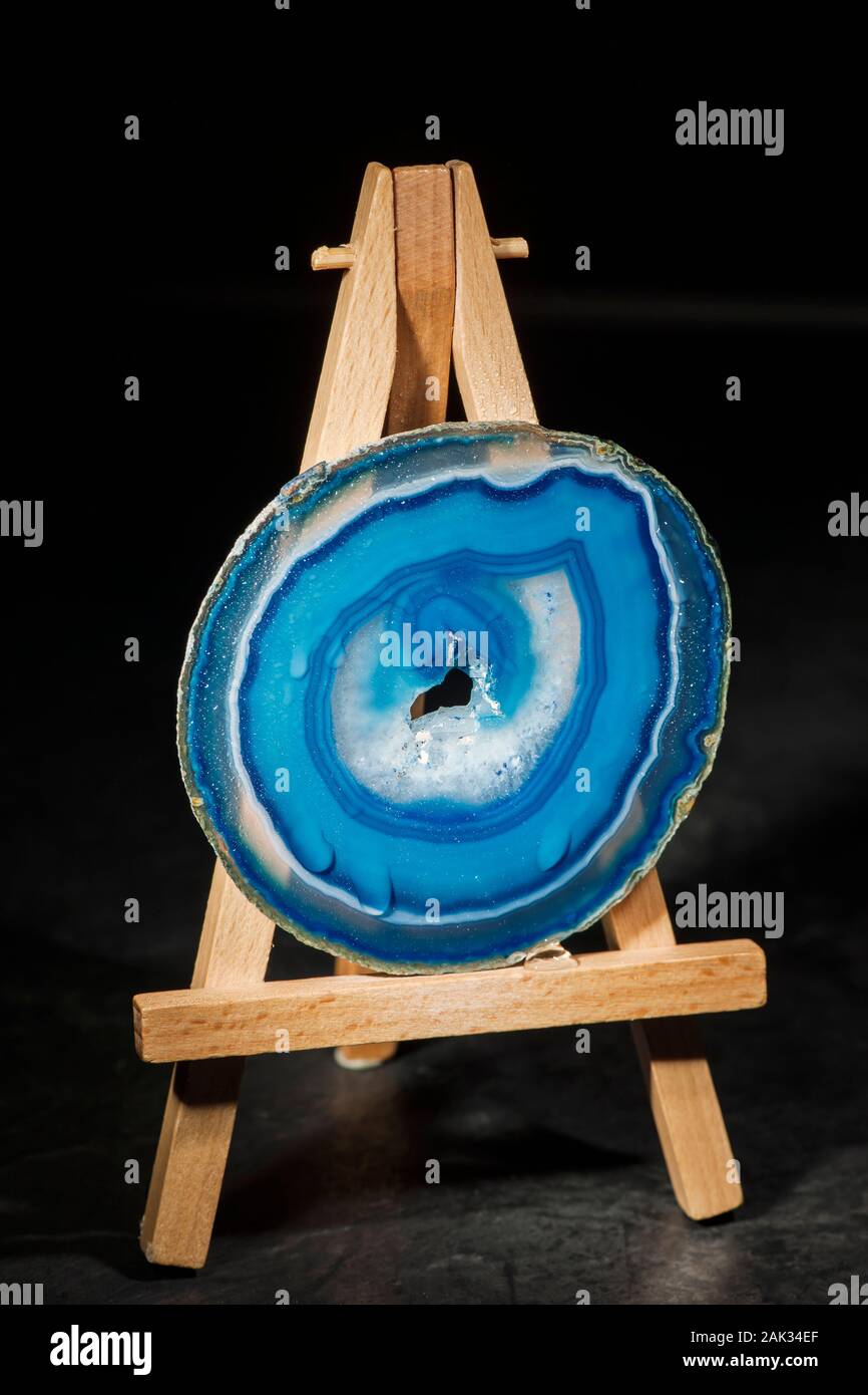 Studio shot of a round, thin, polished and blue-banded agate disc with druse (hole in the middle part) standing dripping wet on a miniature easel in t Stock Photo