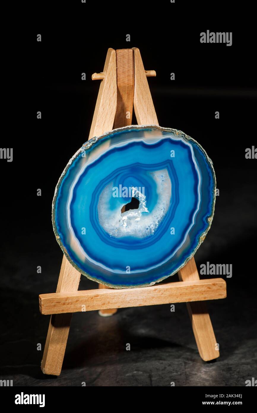 Studio shot of a round, thin polished and blue banded agate slice with druse (hole in the middle part) standing in the front light on a miniature ease Stock Photo