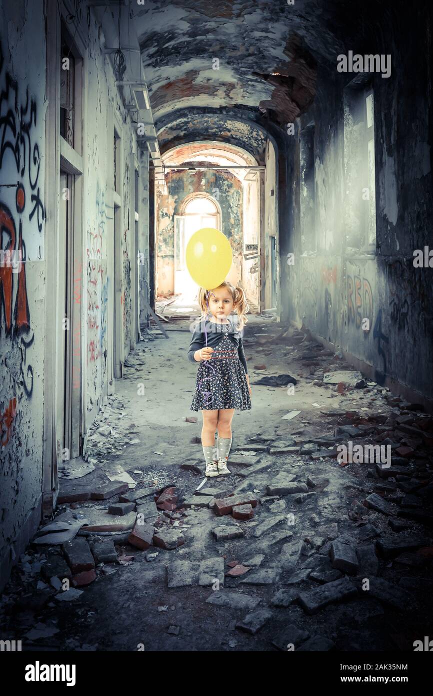 portrait of a 3 year old blonde girl with a balloon inside a decadent and abandoned building. Loneliness concept. Stock Photo