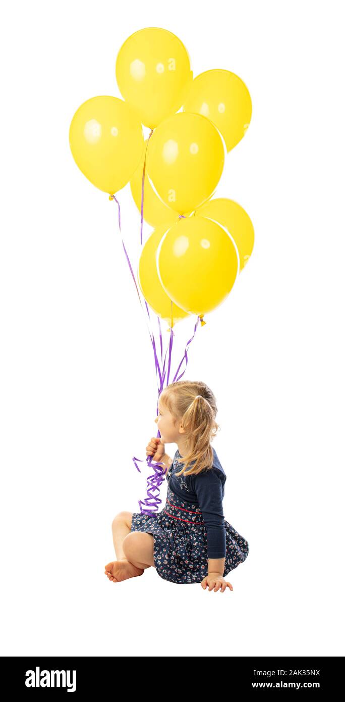 portrait of a sitting 3 year old girl holding a group of yellow balloons. side view. isolated on white Stock Photo