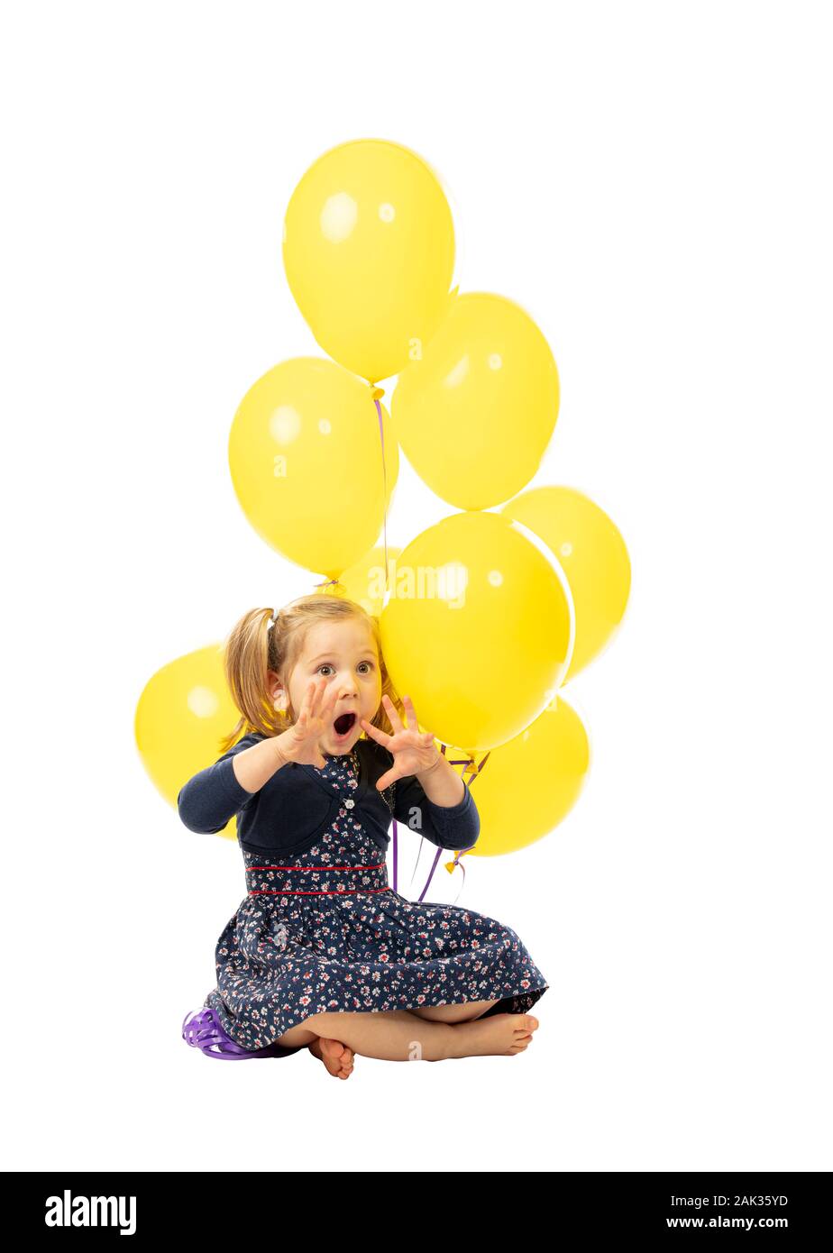 little girl sitting with balloons, playful and surprised expression. isolated on white background. childhood concept. Stock Photo