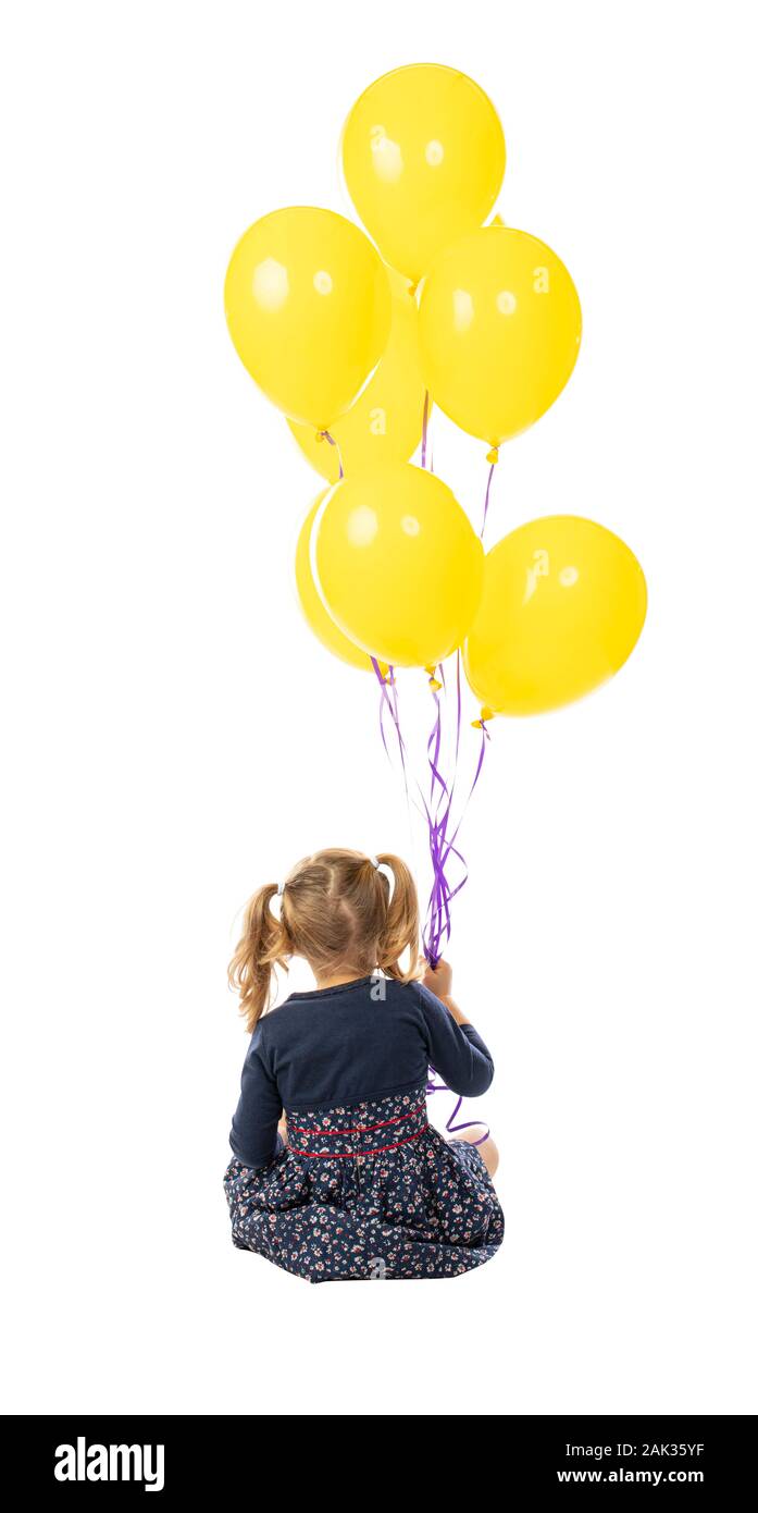 portrait of a sitting 3 year old girl holding a group of yellow balloons. seen from behind. isolated on white Stock Photo