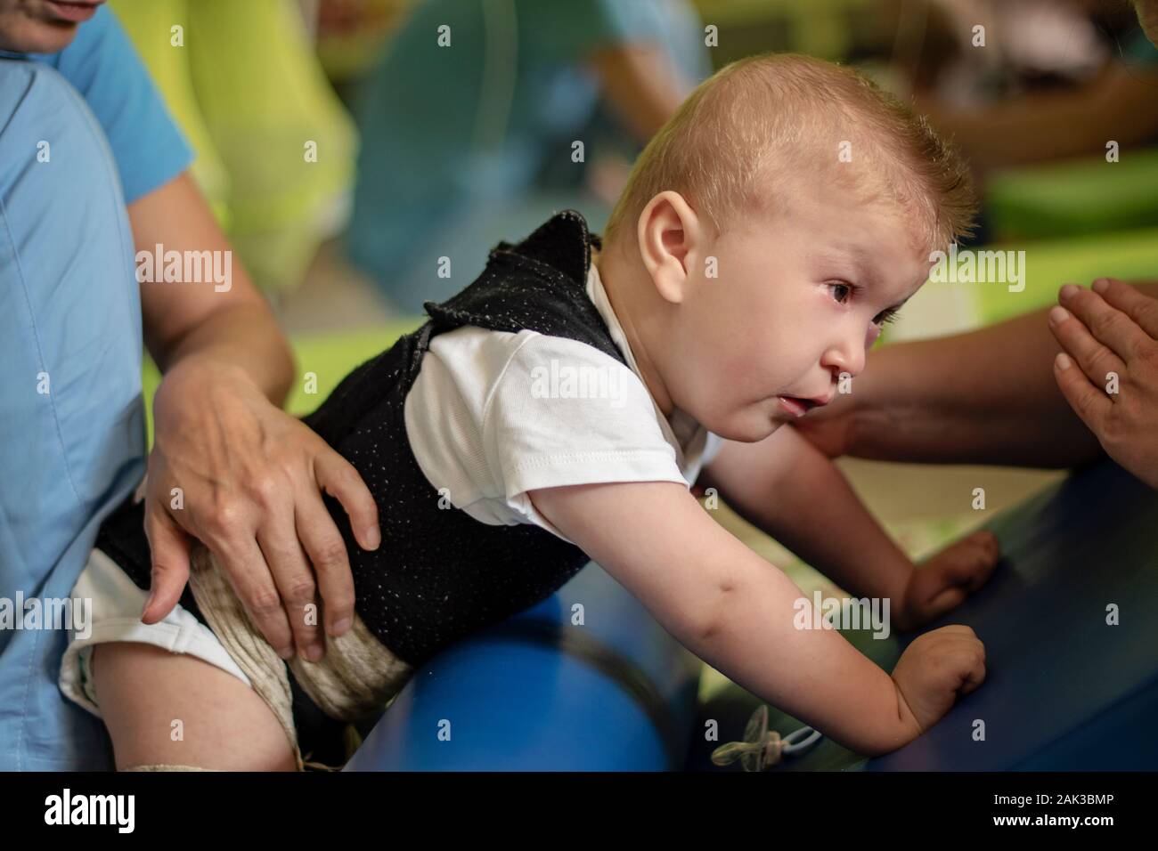 Portrait of a baby with cerebral palsy on physiotherapy in children therapy center. Boy with disability has therapy by doing exercises. Special needs. Stock Photo