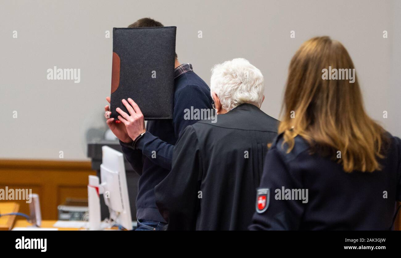 07 January 2020, Lower Saxony, Lüneburg: The defendant (l) stands with a folder in front of his face next to Herbert Lederer (M), his lawyer, in the Lüneburg Regional Court before the start of the trial. The 26-year-old is alleged to have sexually abused several children in Lueneburg and other places as trainer and supervisor of a DLRG local group. Photo: Philipp Schulze/dpa Stock Photo