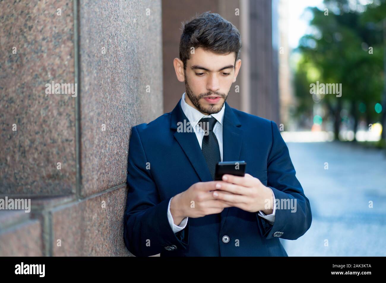 Hipster businessman with beard and suit sending message outdoor in summer in city Stock Photo