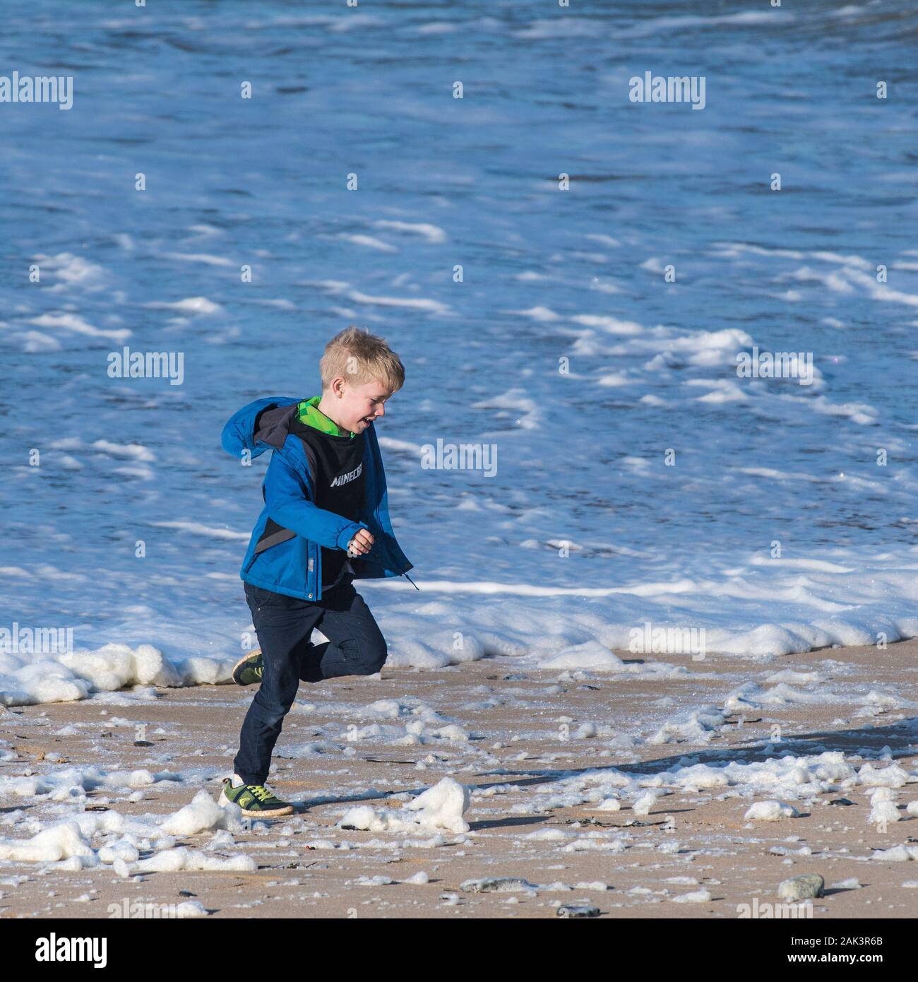A young boy having fun running through the spume blown onto Fistral Beach in Newquay in Cornwall. Stock Photo