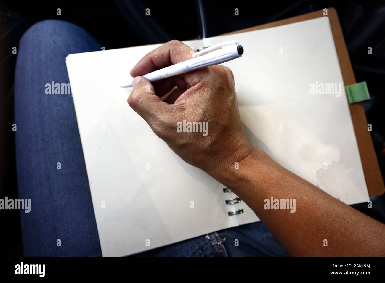 Photo of a hand writing with a pen on a notebook while inside a car Stock Photo
