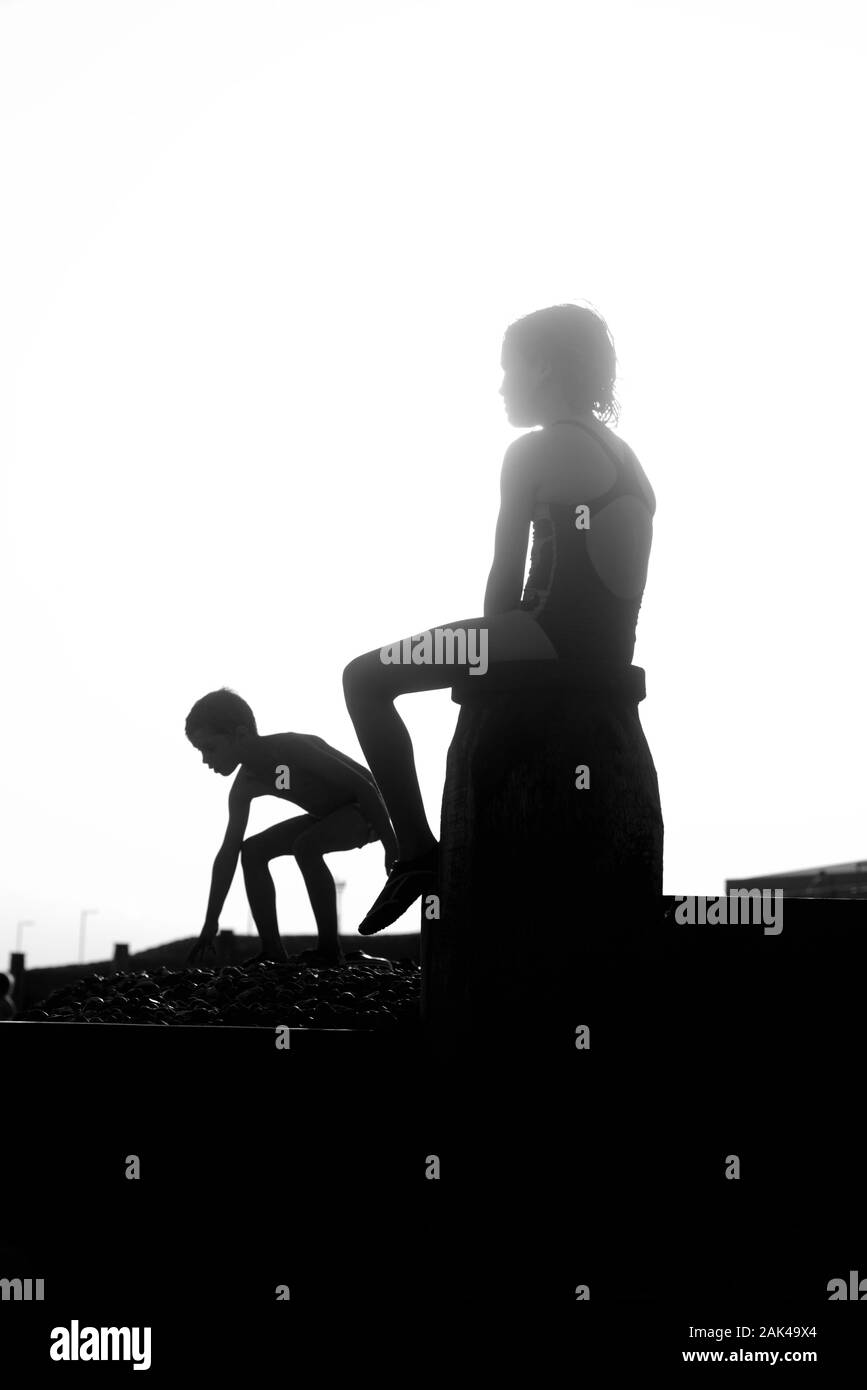 Silhouetted children playing on the groynes at Southwick Beach, Brighton & Hove Stock Photo