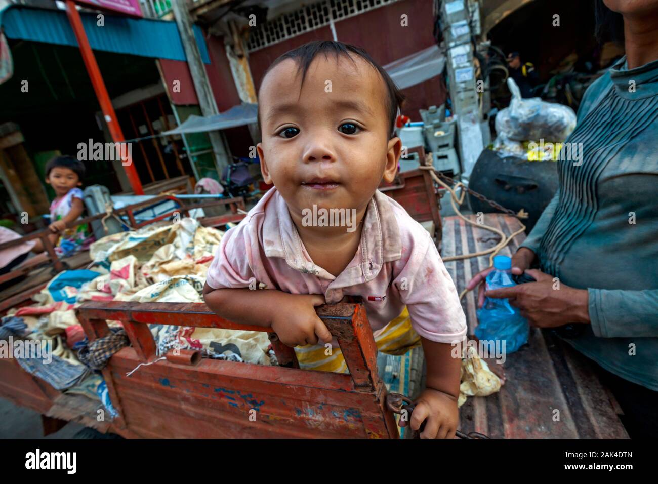 A poor toddler whose homeless family scavenges for recyclable material sits a vehicle used to transport recyclables in Kampong Cham, Cambodia. Stock Photo