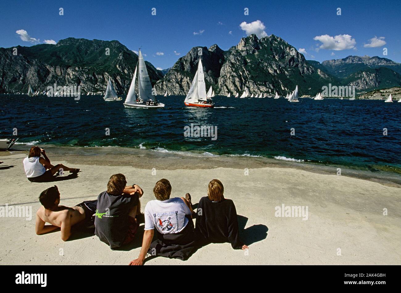 A group of young people stting at a beach in Nago-Torbole at the northern lakefront of Lake Garda, the largest lake of Italy, that is situated in the Stock Photo