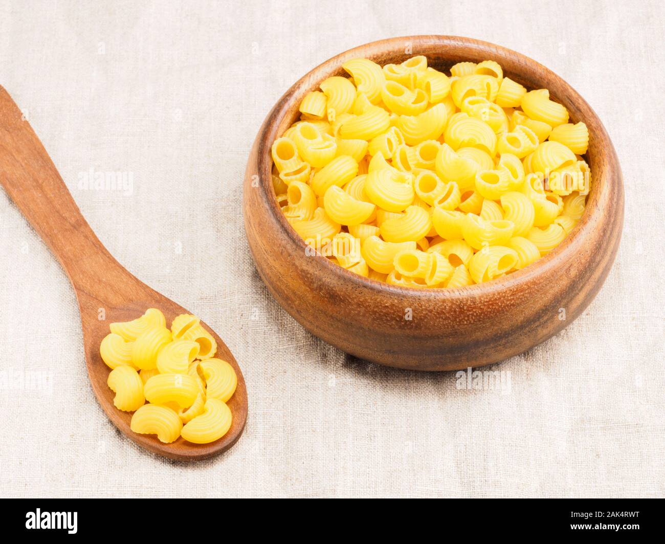 Pasta helices type in wooden bowl and spoon on a beige fabric background. Healthy eating concept Stock Photo