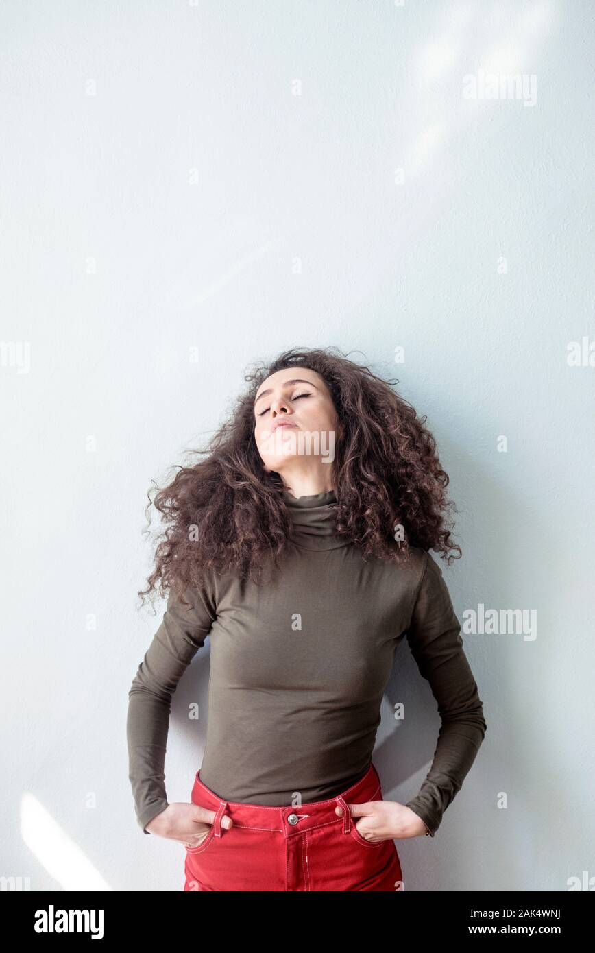 Young woman with curly hair in casual dress against white wall released Stock Photo