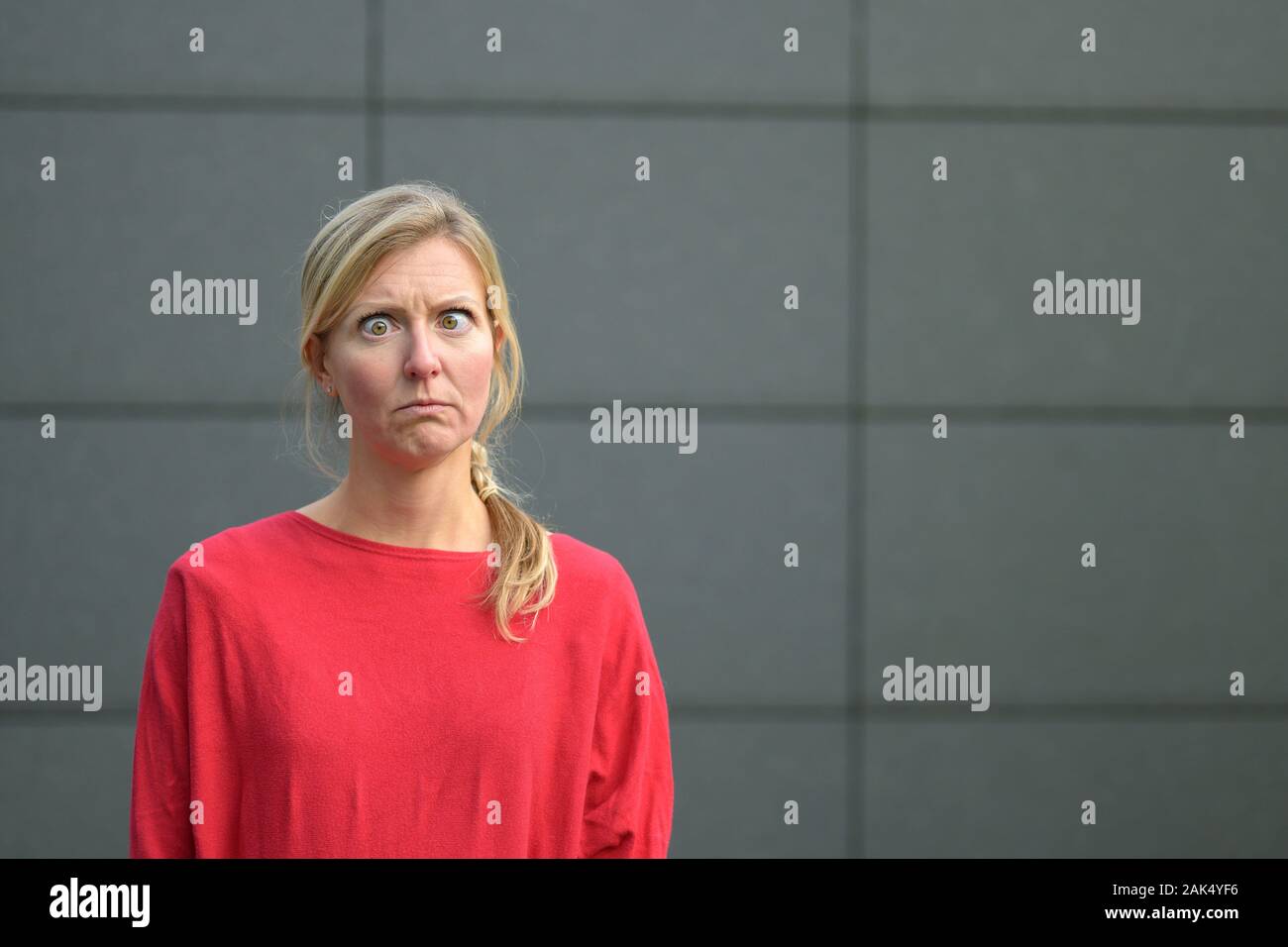 Angry woman staring wide eyed at the camera with a fierce grumpy expression against a grey wall Stock Photo