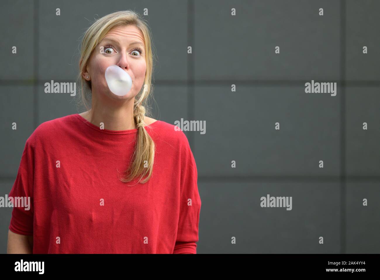 Blond woman blowing a bubble with bubblegum inflating it from her mouth ...