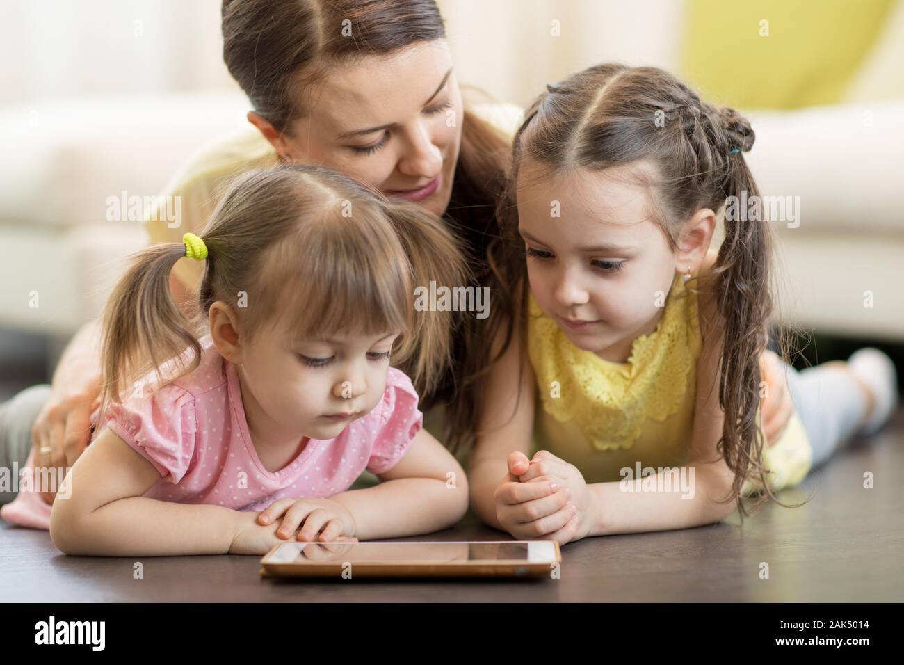 Preschool children and their mom lying on floor in living room with tablet pc Stock Photo