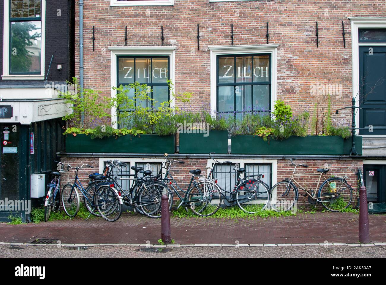 Brick wall building with many bikes parked in front of it and the sidewalk is wet of the rain Stock Photo