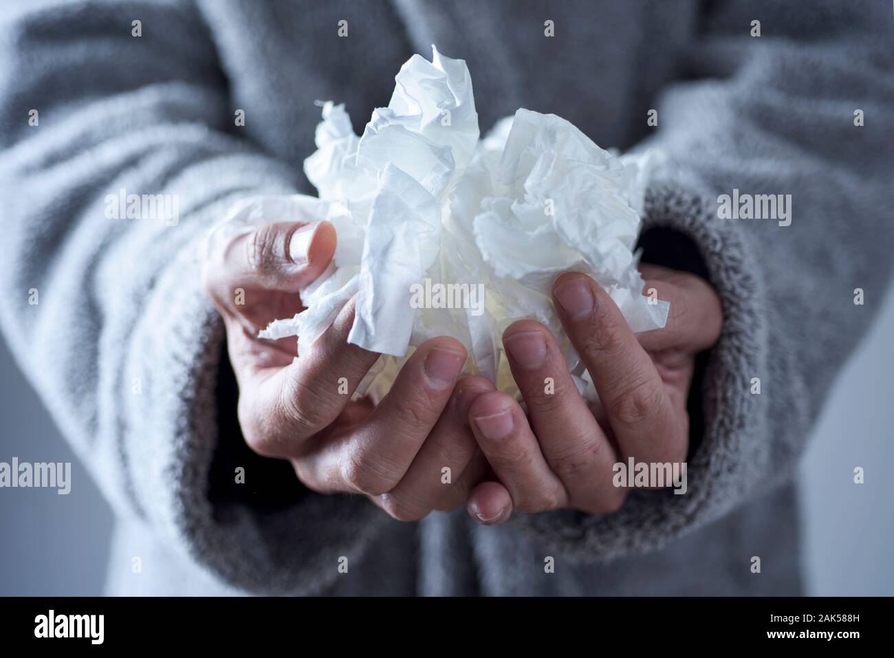closeup of an ill caucasian man at home, wearing a light gray fluffy house robe, with a pile of used tissues in his hands Stock Photo
