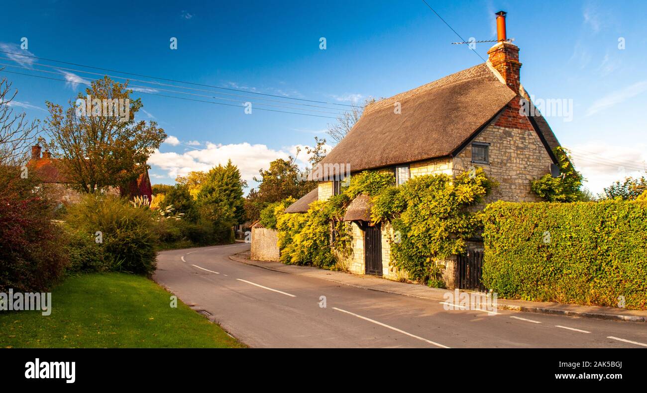 Gillingham, Dorset, UK - October 6, 2012: A traditional thatched-roof stone cottage is covered with summer climbing plants in the village of Fifehead Stock Photo