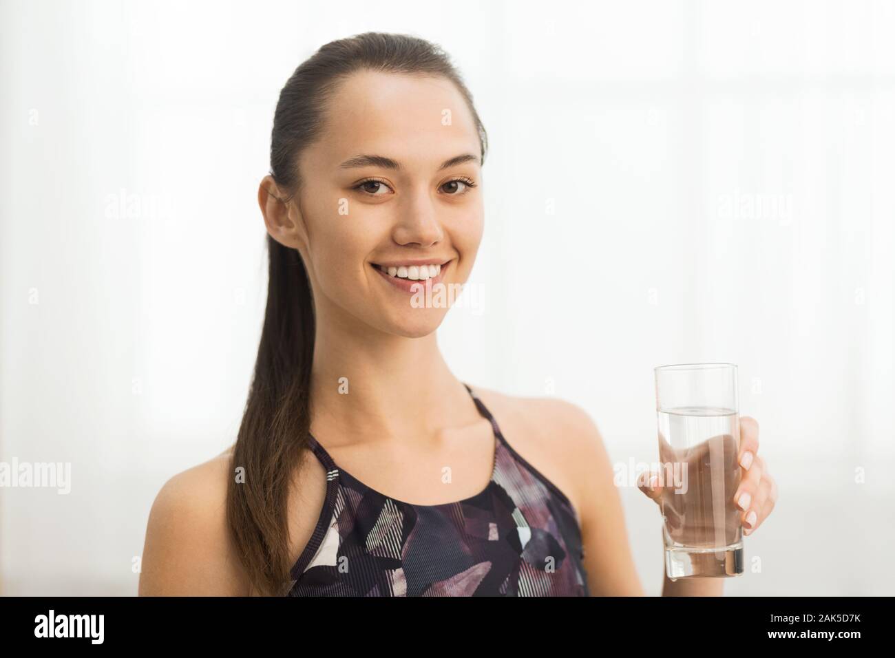 Hydration concept. Girl with glass of water after home workout smiling