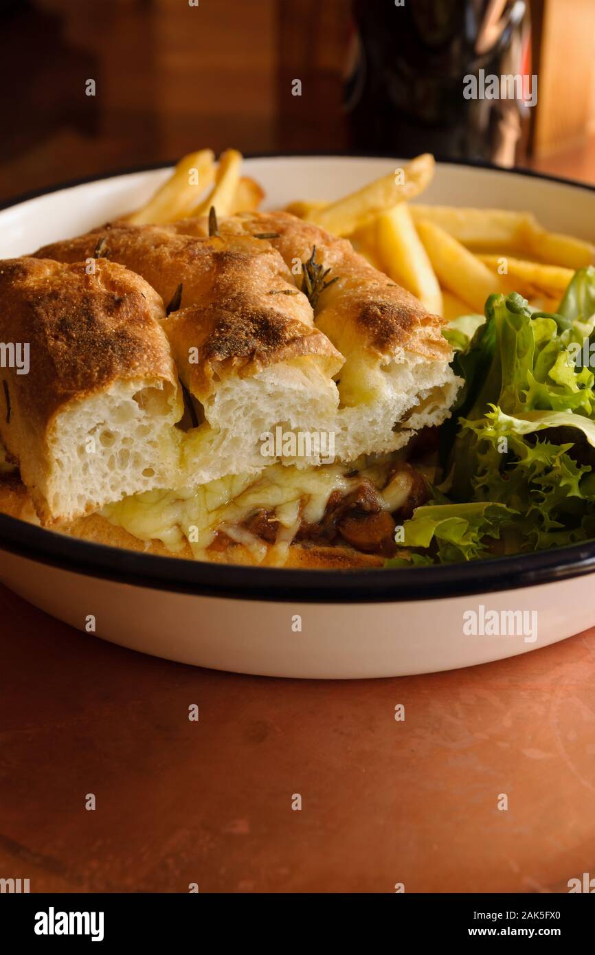 Grilled Focaccia bread sandwich filled with melted cheese sausage and served with French fries and salad Stock Photo
